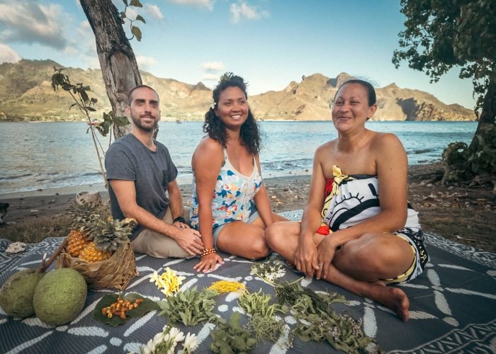 deux femmes polynésiennes avec un touriste assis sur le bord de plage, s'apprenant à confection un kumuhei - slow travel