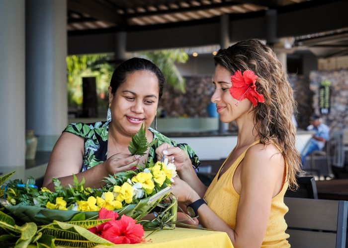 Une femme polynésienne et une touriste confectionnant une couronne de fleurs - slow travel