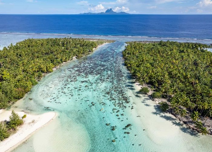 Hôtel Le Taha’a by Pearl Resorts 5*. Vue aérienne sur le jardin de corail de l'hôtel. Océan et île de Bora Bora en arrière plan.