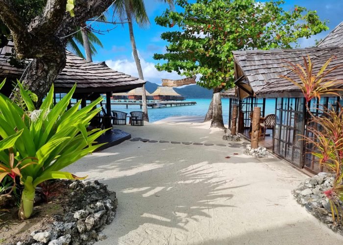 subtiles-tahiti-tahaa-hotel-vahine-island-6©vahine-island Hôtel Vahine Private Island 4* à Taha’a - chemin menant à la plage. Bar et restaurant de part et d'autre. Bungalows sur pilotis et lagon en arrière plan.