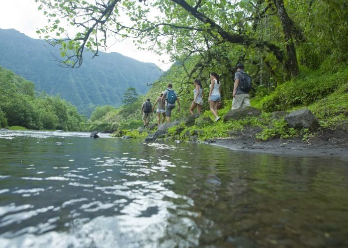 groupe de six randonneurs marchant le long d'une rivière dans la vallée de la papenoo à Tahiti. Montagne verte en arrière plan. Randonnée et Aventure en Polynésie : Les Meilleurs Sentiers et Conseils de Sécurité