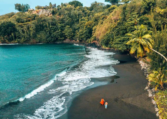 Hôtel Le Tahiti By Pearl Resorts 4* à Tahiti. Vue aérienne sur la plage de sable noir dans la baie de Matavai. Couple marchant sur la plage.