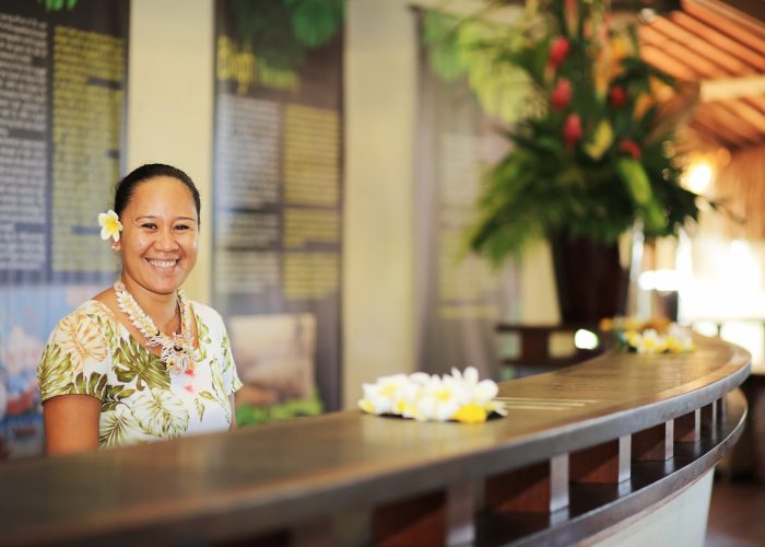 Hôtel Le Tahiti By Pearl Resorts 4* à Tahiti. Réceptionniste tahitienne souriant derrière le deck de la réception. Accueil polynésien.