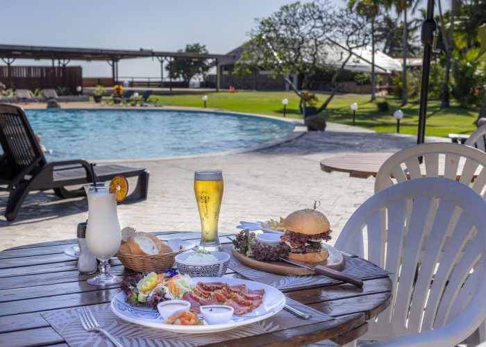 Hôtel Royal Tahitien 3* à Tahiti. Table dressée en extérieur avec poisson cru et hamburger. Piscine en arrière plan.