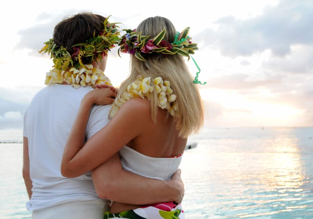 couple de dos avec colliers et couronnes de fleurs à l'hôtel Te Moana Tahiti Resort 3*, regardant le coucher du soleil sur le lagon