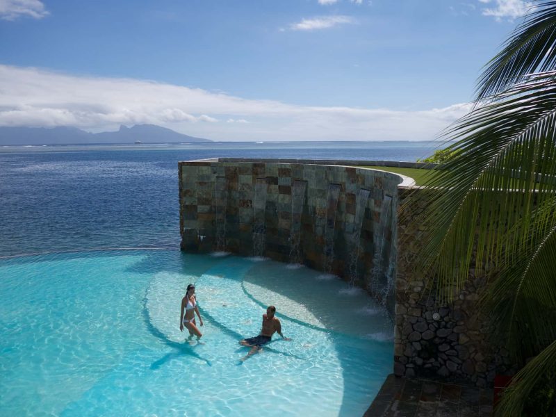 Hôtel Te Moana Tahiti Resort 3*. Vue sur la piscine à débordement avec un couple qui se baigne. Lagon et île de Moorea en arrière plan.