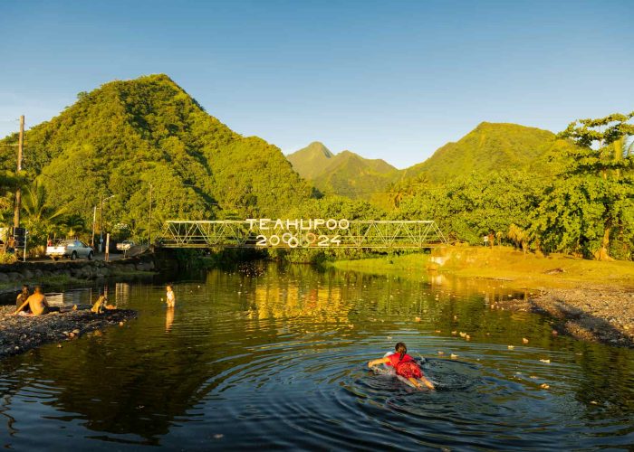 vue du pont de Teahupoo à Tahiti avec surfeuse allongée sur une place et montagne en arrière plan