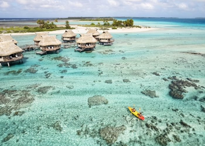 subtiles-tahiti-tikehau-hôtel-le-tikehau-by-pearl-resorts-6©le-tikehau-by-pearl-resorts Hôtel Le Tikehau by Pearl Resorts 4*- vue aérienne d'un couple sur un kayak sur le lagon de Tikehau. Suites sur pilotis et motus.