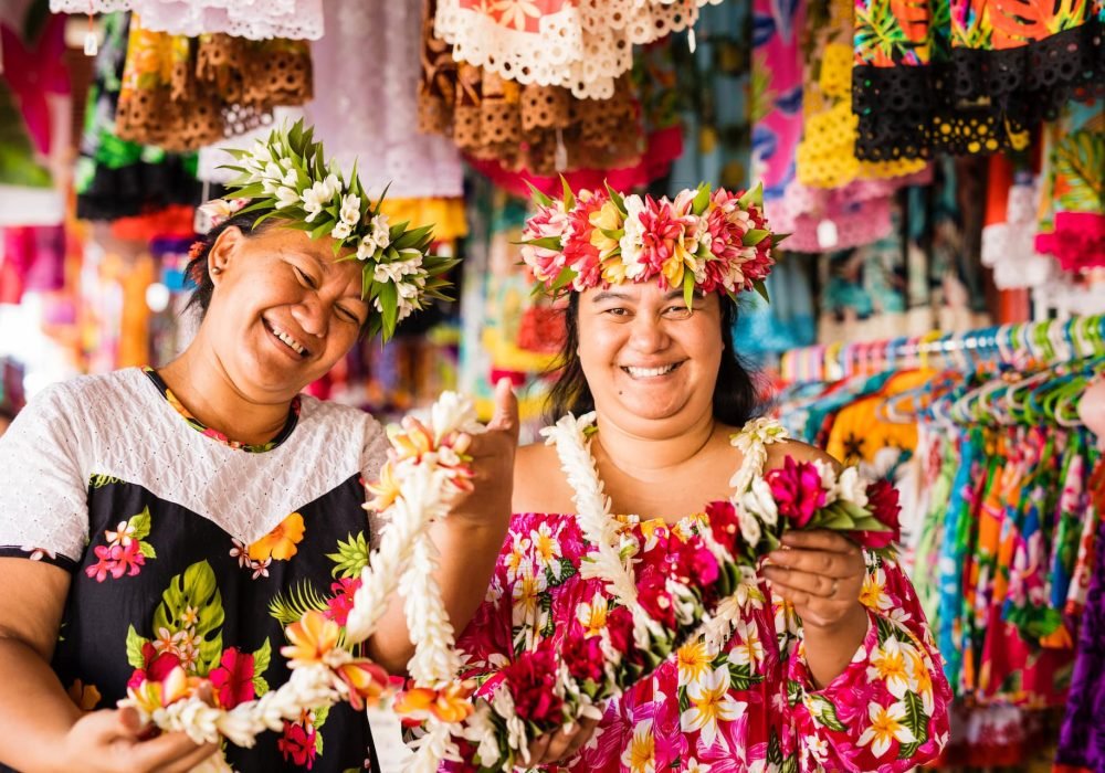 deux femmes polynésiennes portant des couronnes de fleurs sur la tête et des colliers dans les mains au marché local de Papeete